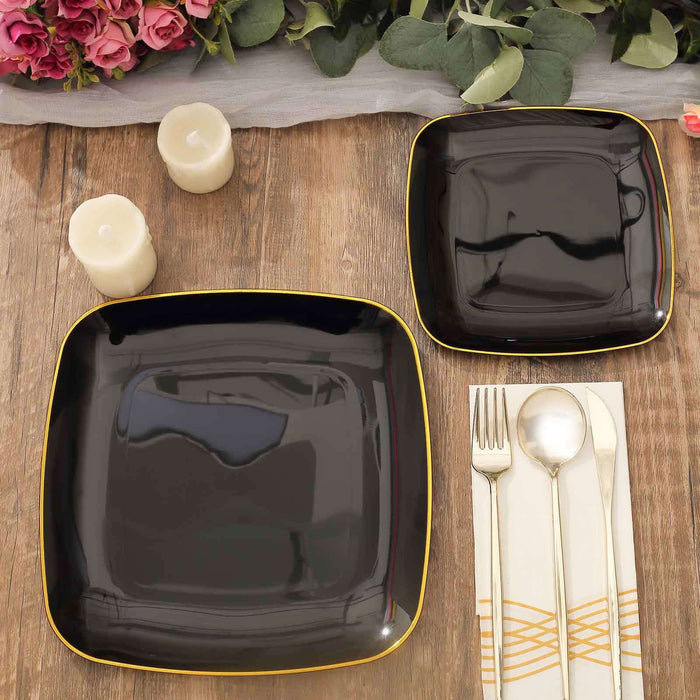 Black square plates with gold trim on a wooden table with candles and floral decor.