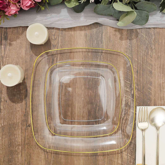Clear square plates with gold trim stacked on a wooden table.