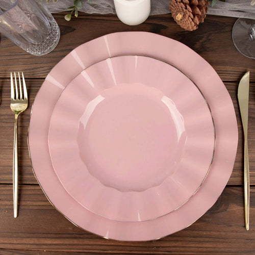 Pink scalloped dinner plates set on a wooden table with gold utensils.