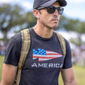 Man wearing GORUCK America shirt, camo rucksack, sunglasses, and cap outdoors