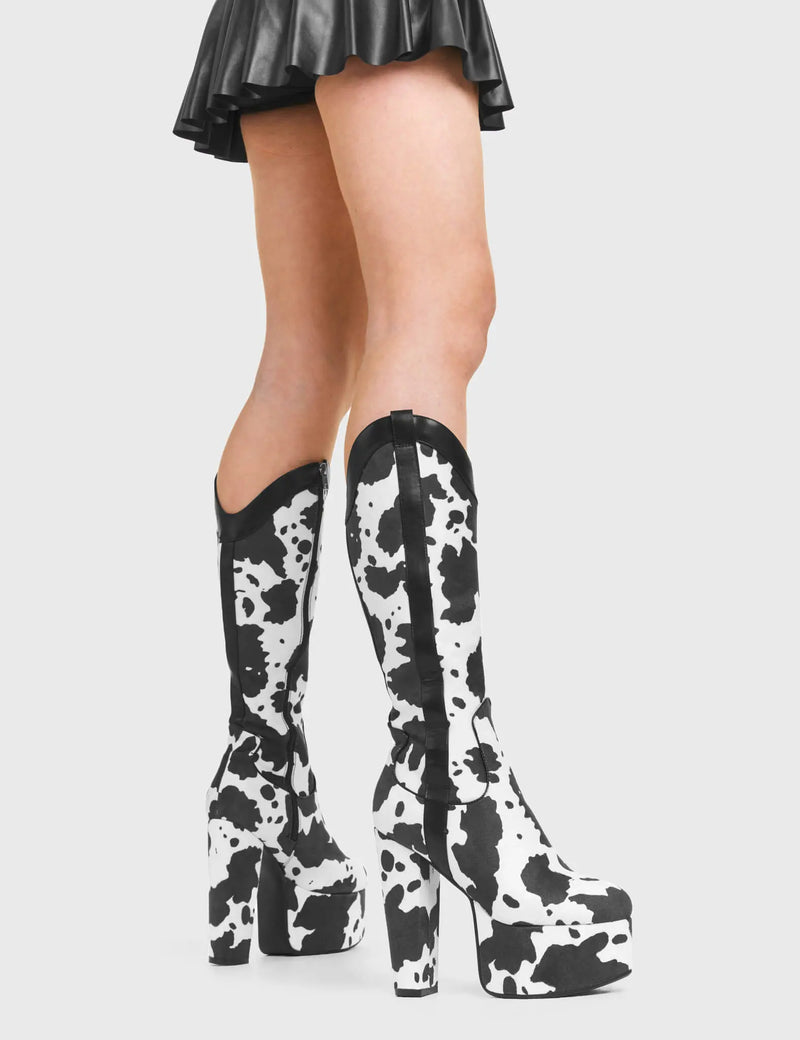THE WILD ICON
  
  Cowgirl Platform Knee High Boots in Cow Print faux suede. These vegan Platform Boots feature an ICONIC western cow print and High Platform sole and heel, the only choice for festival goers. Made with eco-friendly materials and 100% cruelty-free, these boots are as ethical as they are wild!
  
  
  - Platform Height: 2.5 inch
  - Heel Height: 5.5 inch 
  - Knee High length
  - Black zipper 
  - Western neck
  - Platform sole
  - Pointed toe 
  - 100% vegan 
  
  SKU: LMF 376 - White Cow
