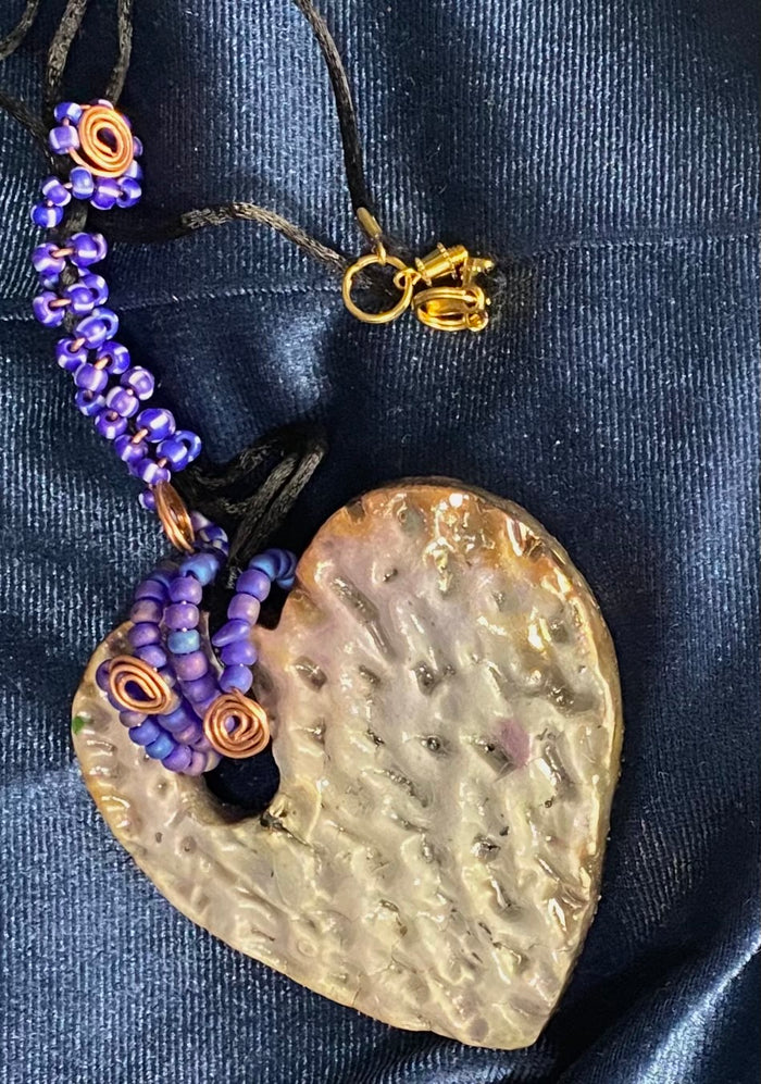 Have A Heart ! Each heart pendant is handmade with love! It is 3"x 3" and weighs approx. 3ozs. This pendant has a white metallic raku glazes that renders a unique translucent  patina. The heart has a textured pattern . It holds a spiral of blue mini beads on a spiral copper wire. This pendant has a nice 12" black suede cord!