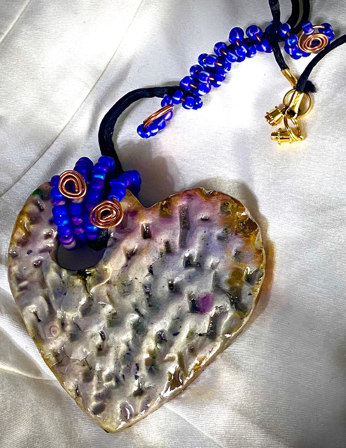 Have A Heart ! Each heart pendant is handmade with love! It is 3"x 3" and weighs approx. 3ozs. This pendant has a white metallic raku glazes that renders a unique translucent  patina. The heart has a textured pattern . It holds a spiral of blue mini beads on a spiral copper wire. This pendant has a nice 12" black suede cord!