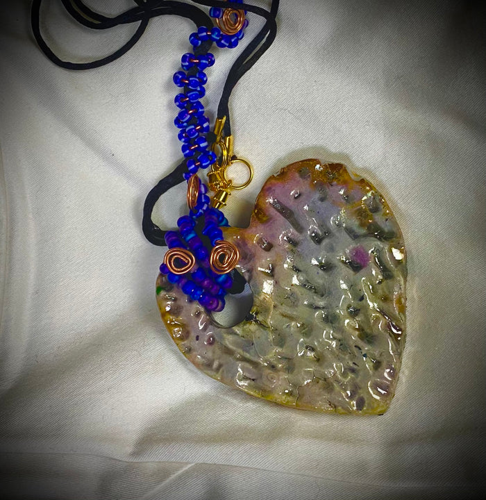 Have A Heart ! Each heart pendant is handmade with love! It is 3"x 3" and weighs approx. 3ozs. This pendant has a white metallic raku glazes that renders a unique translucent  patina. The heart has a textured pattern . It holds a spiral of blue mini beads on a spiral copper wire. This pendant has a nice 12" black suede cord!