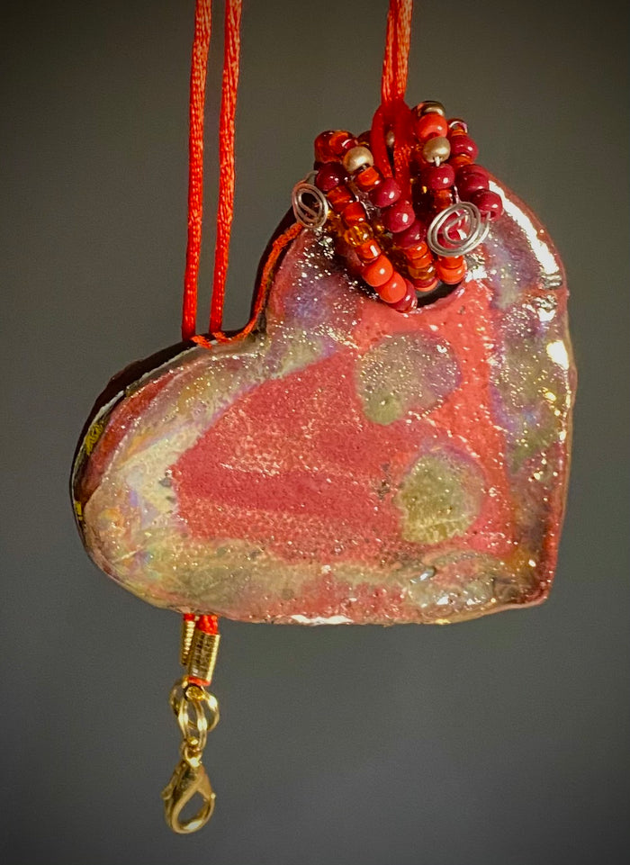 Have A Heart ! Each heart pendant is handmade with love! It is 3"x 3" and weighs approx. 3ozs. This pendant has a red violet and gold metallic raku glazes that renders a unique translucent  patina. The heart has a textured pattern . Both sides are  are different and equally beautiful! It holds a spiral of red violet mini beads on a spiral copper wire. This pendant has a nice 12" red suede cord!