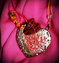 Have A Heart ! Each heart pendant is handmade with love! It is 3"x 3" and weighs approx. 3ozs. This pendant has a red violet and gold metallic raku glazes that renders a unique translucent  patina. The heart has a textured pattern . Both sides are  are different and equally beautiful! It holds a spiral of red violet mini beads on a spiral copper wire. This pendant has a nice 12" red suede cord!