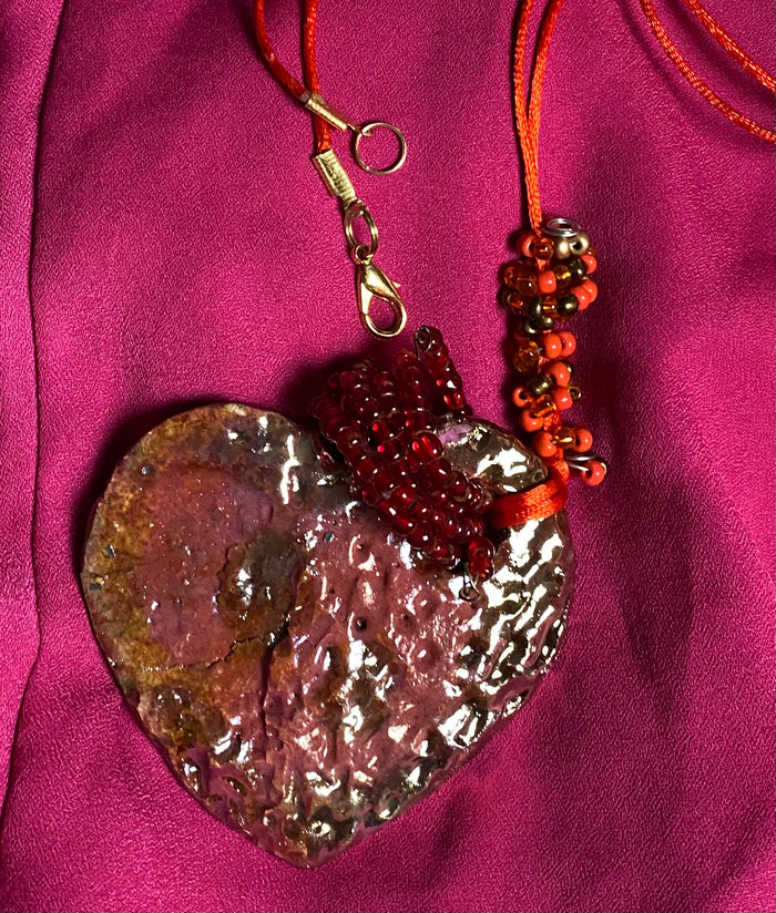 Have A Heart ! Each heart pendant is handmade with love! It is 3"x 3" and weighs approx. 3ozs. This pendant has a red violet and gold metallic raku glazes that renders a unique translucent  patina. The heart has a textured pattern . Both sides are  are different and equally beautiful! It holds a spiral of red violet mini beads on a spiral copper wire. This pendant has a nice 12" red suede cord!