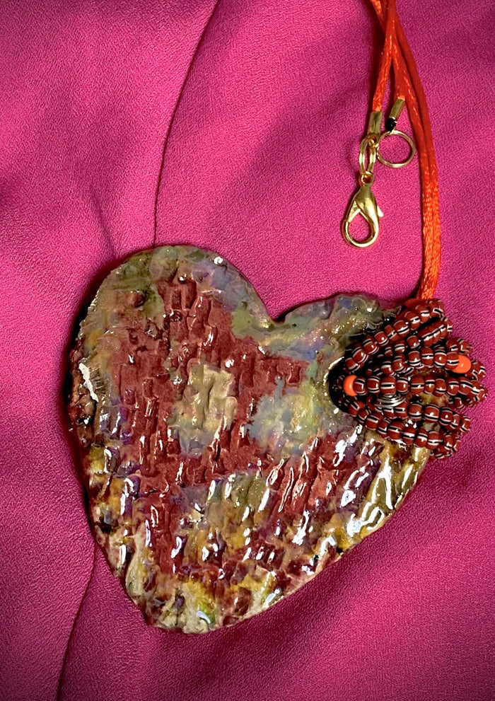 Have A Heart ! Each heart pendant is handmade with love! It is 3"x 3" and weighs approx. 3ozs. This pendant has a red violet and gold metallic raku glazes that renders a unique translucent  patina. The heart has a textured pattern . Both sides are  are different and equally beautiful! It holds a spiral of red violet mini beads on a spiral copper wire. This pendant has a nice 12" red suede cord!