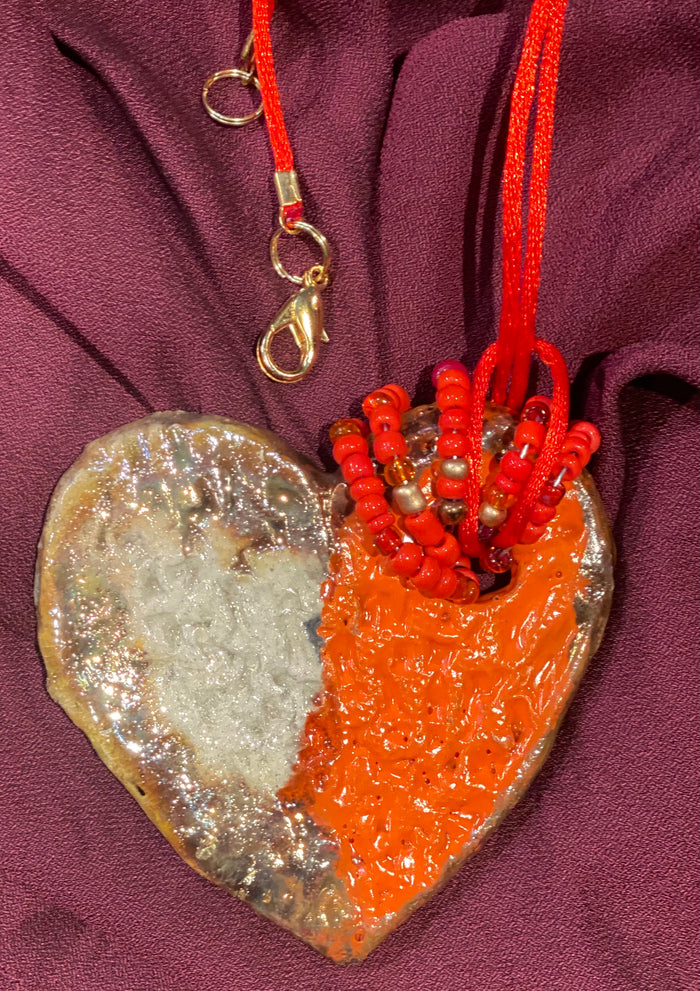 Have A Heart ! Each heart pendant is handmade with love! It is 3"x 3"and weighs approx. 3ozs. This pendant has a red violet and gold metallic raku glazes that renders a unique translucent  patina. The heart has a textured pattern . Both sides are  are different and equally beautiful! It holds a spiral of red and gold mini beads on a spiral copper wire. This pendant has a nice 12" red rattail cord!