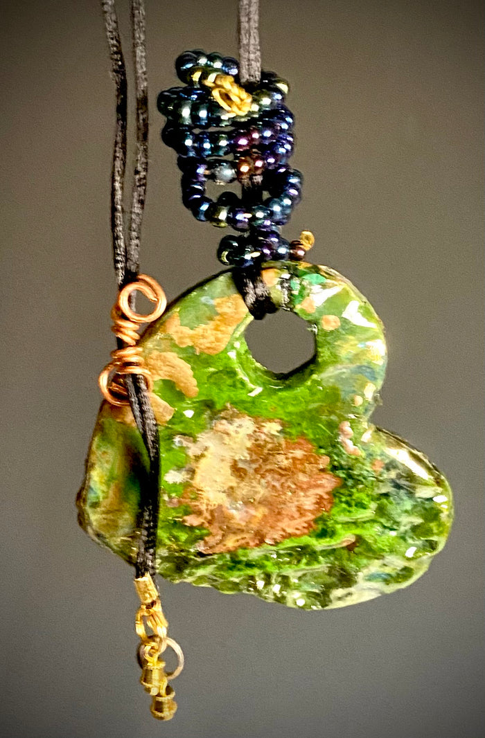 Have A Heart ! Each heart pendant is handmade with love! It is 3"x 3" and weighs approx. 3ozs. This pendant has a green and gold metallic raku glazes that renders a unique translucent  patina. The heart has a textured pattern . Both sides are  are different and equally beautiful! It holds a spiral of multicolored mini beads on a spiral golden wire. This pendant has a nice 12" black rattail cord!