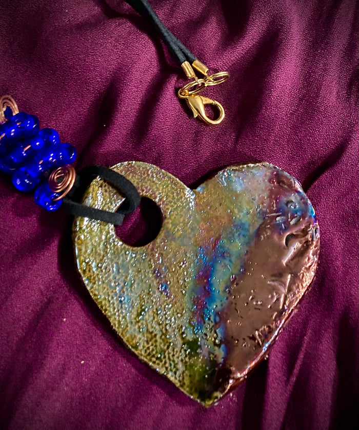 Have A Heart ! Each heart pendant is handmade with love! It is 3"x 3" and weighs approx. 3ozs. This pendant has a toasty copper metallic raku glazes that renders a unique translucent patina. The heart has a textured pattern . Both sides are  are different and equally beautiful! It holds a spiral of red violet mini beads on a spiral copper wire. This pendant has a nice 12"  black suede cord!
