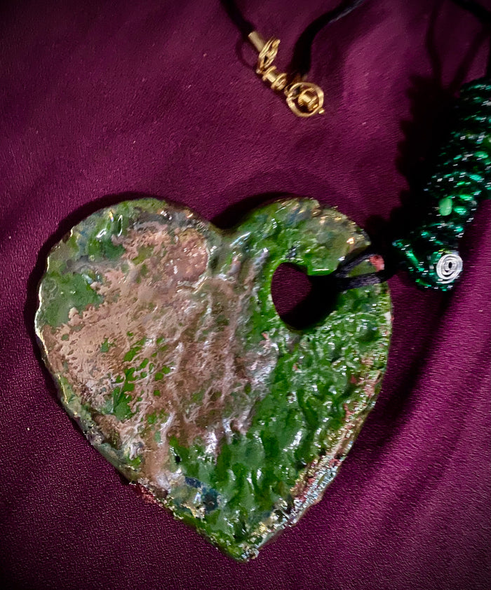 Have A Heart ! Each heart pendant is handmade with love! It is 3"x 3" and weighs approx. 3ozs. This pendant has a green and copper metallic raku glazes that renders a unique translucent  patina. The heart has a textured pattern . Both sides are  are different and equally beautiful! It holds a spiral of multicolored mini beads on a spiral golden wire. This pendant has a nice 12" black rattail cord!