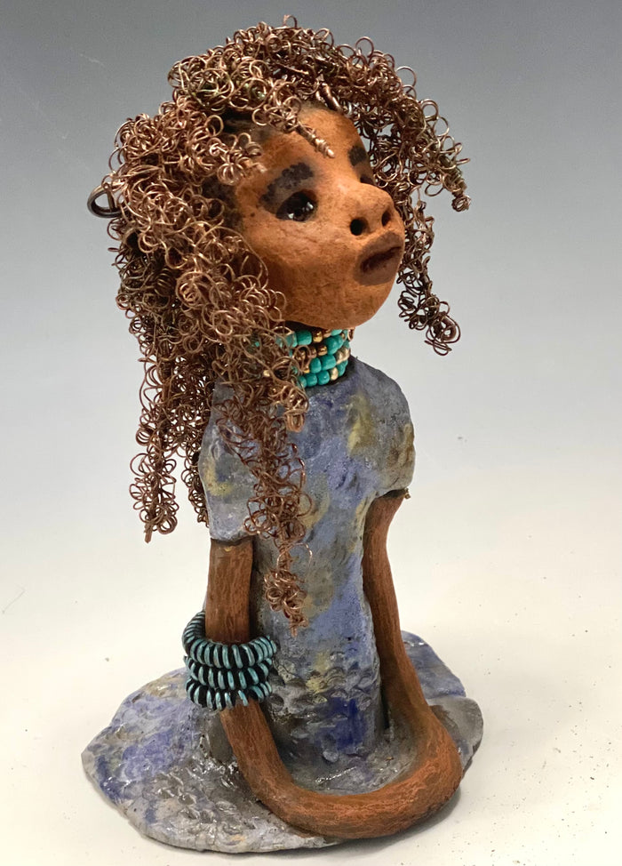 Meet Janae'! She has grown a head full of Hair! Janae' stands 8" x 5" x 4" and weighs 1.03 lbs. She has a lovely honey brown complexion with lovely reddish brown lips. Janae' wears a clay braided hairstyle. Janae' has a colorful metallic blue and gold glazed dress. She wears a blue and antique copper  beaded necklace. With eyes wide opened, Janae' has hopes of finding a new home.