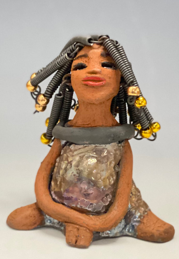 Meet Sadie  Sadie stands 5.5" x 4" x 3" and weighs 8.7 ozs. She wears a lovely glossy  metallic gold dress.. Sadie has over15 feet of coiled wire hair. Sadie appears to sit in a yoga pose. Her long arms rest at her side. Sadie is a great starter piece from the Herdew Collection!