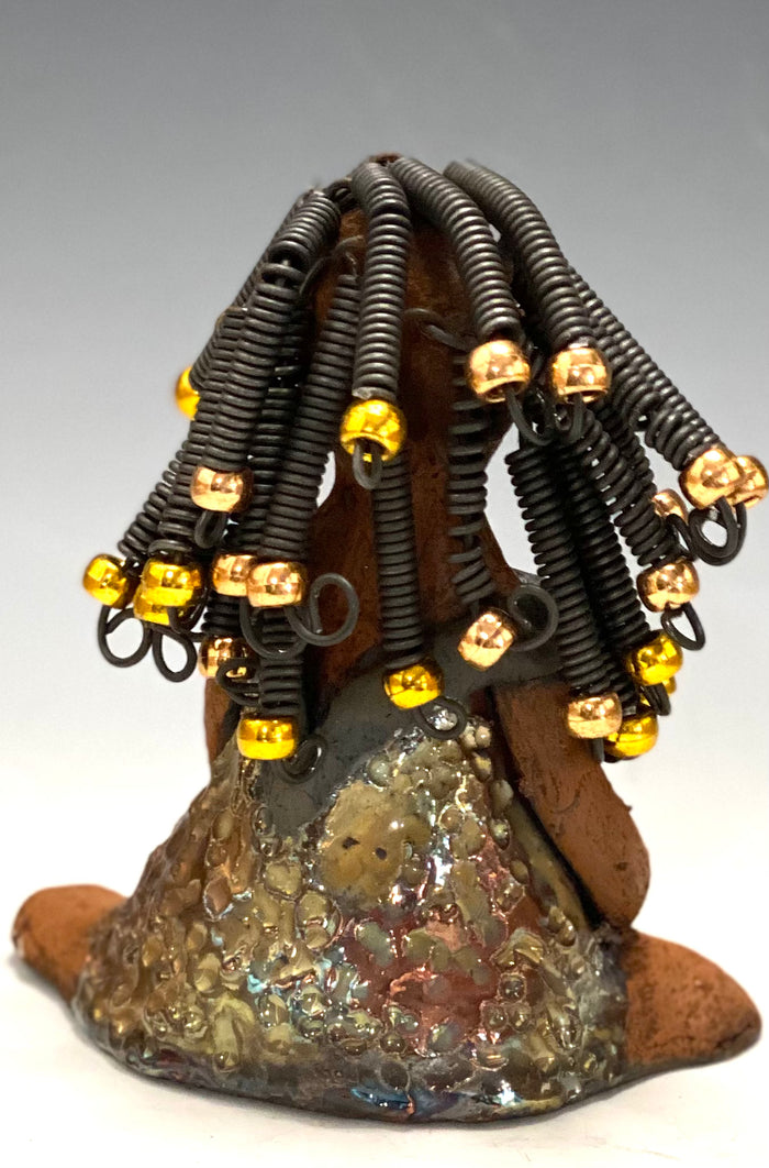 Meet Sadie  Sadie stands 5.5" x 4" x 3" and weighs 8.7 ozs. She wears a lovely glossy  metallic gold dress.. Sadie has over15 feet of coiled wire hair. Sadie appears to sit in a yoga pose. Her long arms rest at her side. Sadie is a great starter piece from the Herdew Collection!