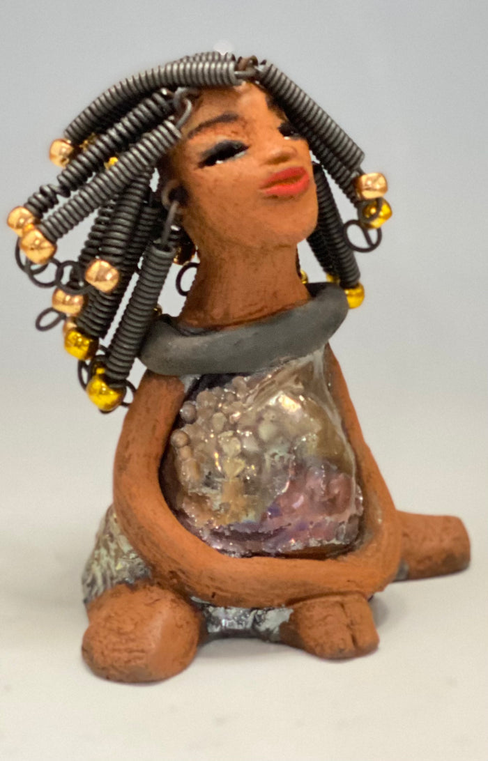 Meet Sadie  Sadie stands 5.5" x 4" x 3" and weighs 8.7 ozs. She wears a lovely glossy  metallic gold dress.. Sadie has over15 feet of coiled wire hair. Sadie appears to sit in a yoga pose. Her long arms rest at her side. Sadie is a great starter piece from the Herdew Collection!