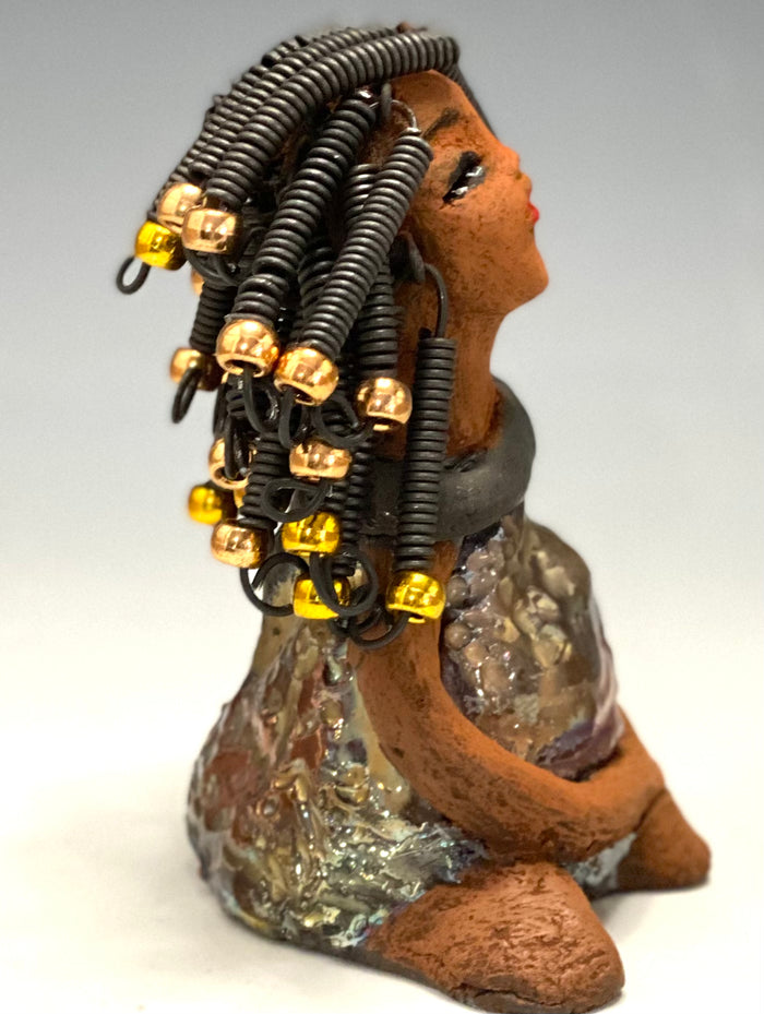 Meet Sadie  Sadie stands 5.5" x 4" x 3" and weighs 8.7 ozs. She wears a lovely glossy  metallic gold dress.. Sadie has over15 feet of coiled wire hair. Sadie appears to sit in a yoga pose. Her long arms rest at her side. Sadie is a great starter piece from the Herdew Collection!