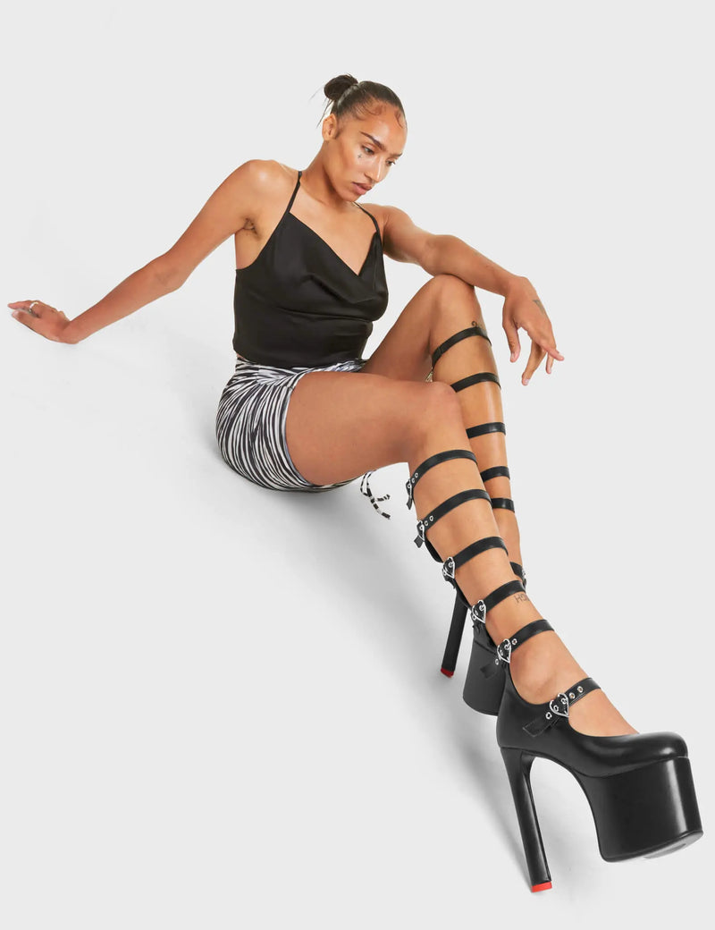 ROYAL TEA
  
  Still Reigning Platform Knee High Boots in Black faux leather. These vegan Boots feature siz adjustable white straps with silver heart shaped buckles and silver eyelets with high heel that features a red heart at the bottom. Walk like royalty.
  
  - Platform Height: 6 CM
  - Heel Height: 14 CM
  - Six Adjustable Straps
  - Cut-out Design
  - Knee High Length
  - Silver Heart Buckles
  - Silver Eyelets
  - Platform Sole
  - Round Toe
  - 100% Vegan
  
  SKU: LMF 4645 - BlackPU